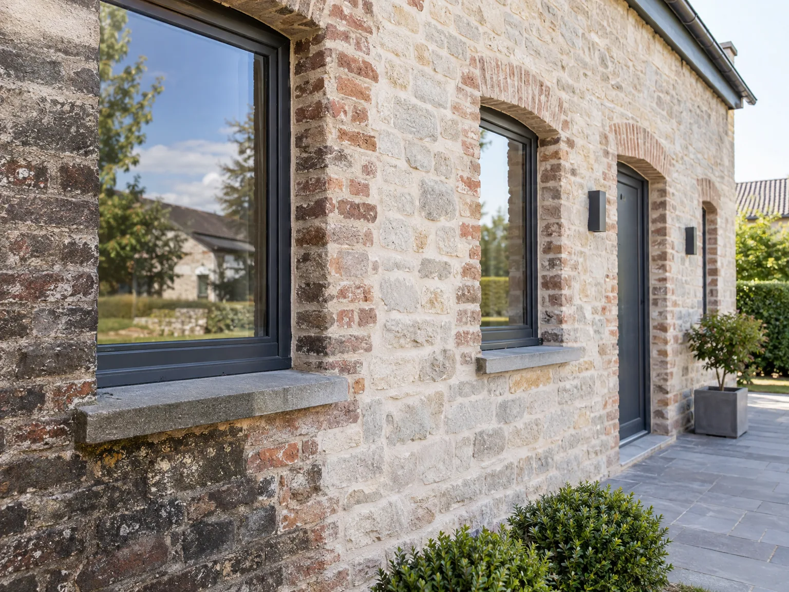 Façade en pierre et brique récemment restaurée avec fenêtres modernes et parapets en pierre